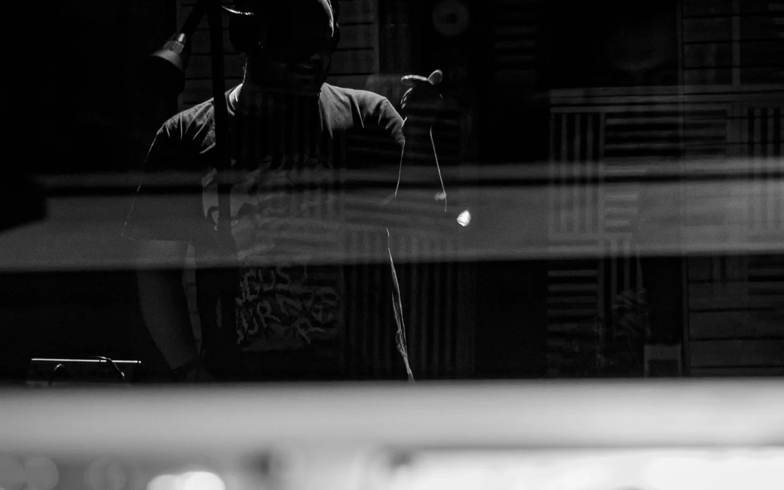 Musicista in cuffia che registra una canzone al microfono in un moderno studio musicale, visto attraverso il vetro.