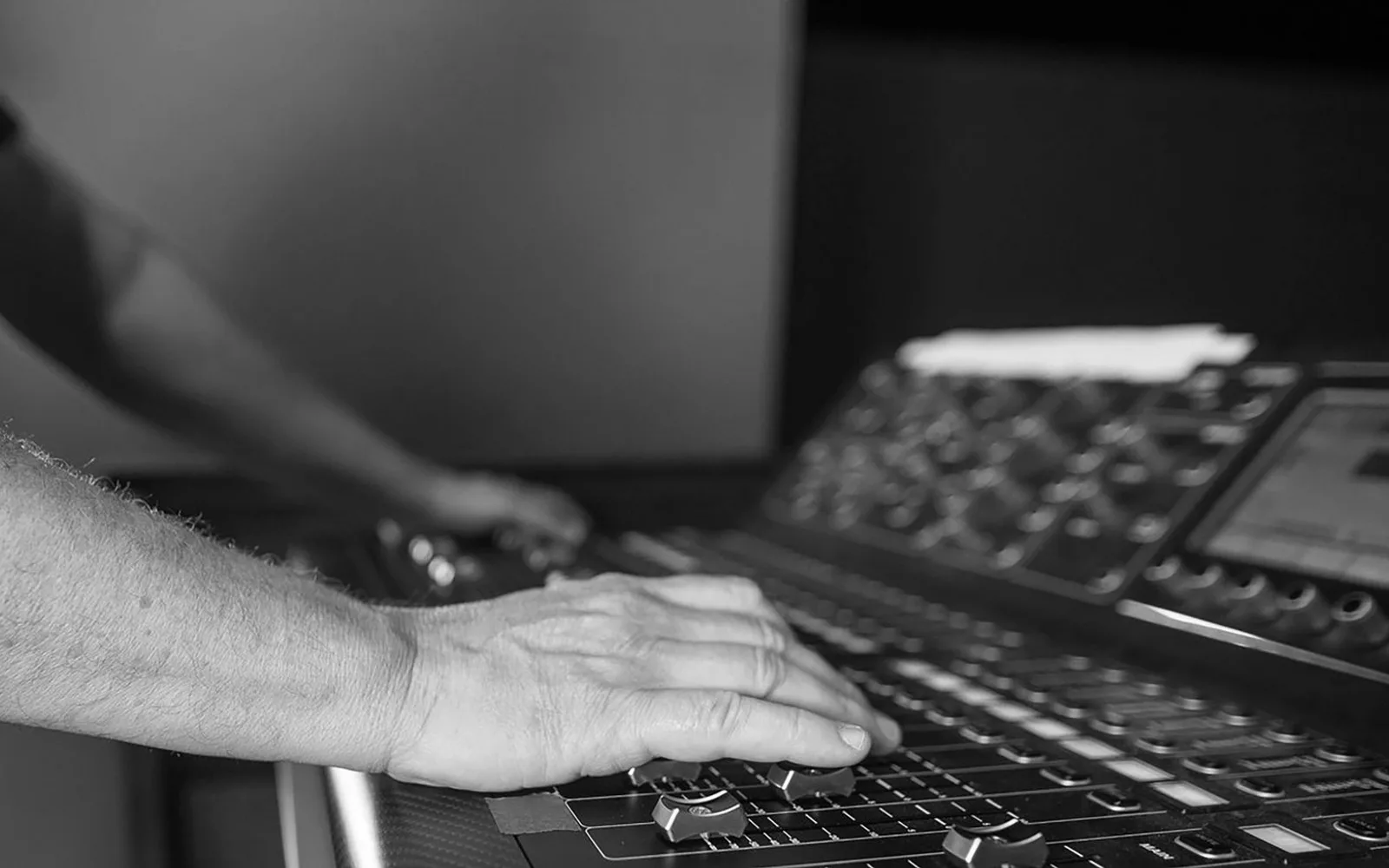 Mani di un tecnico del suono che regola i livelli su un mixer audio in uno studio di registrazione professionale