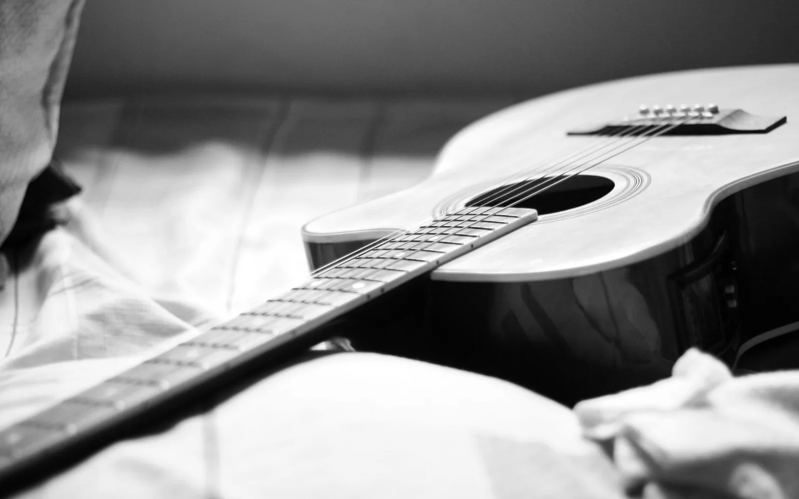 Primo piano di una chitarra acustica appoggiata su un letto in una fotografia in bianco e nero