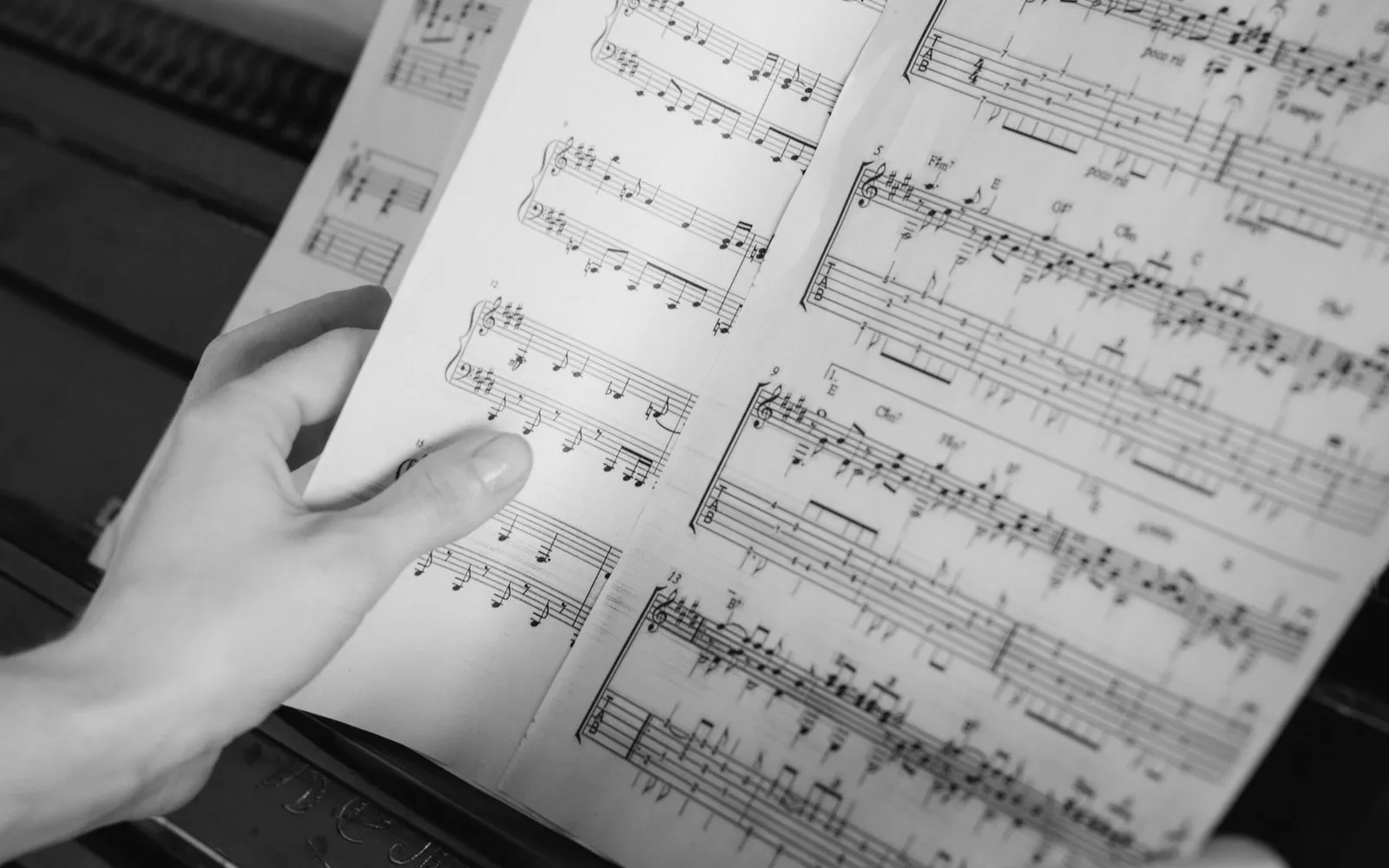 Primo piano di mani che girano pagine di spartiti su tasti di pianoforte. Focus musicale