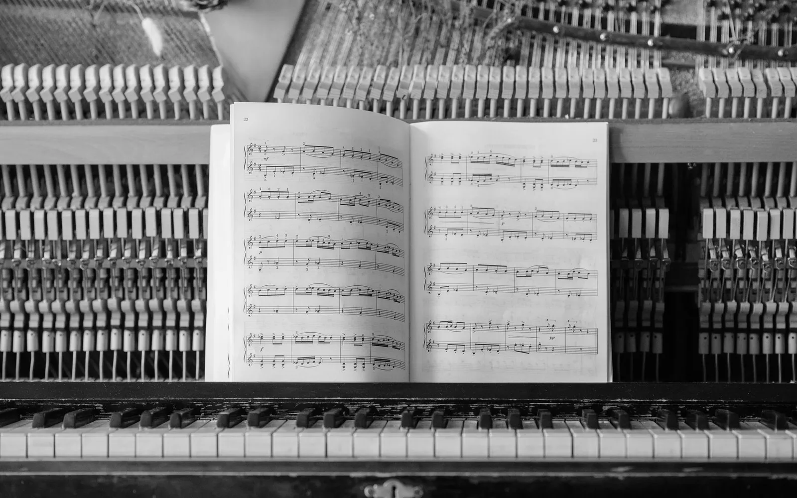 Vista dettagliata degli interni di un pianoforte con spartito posizionato sui tasti, che mostra i meccanismi intricati