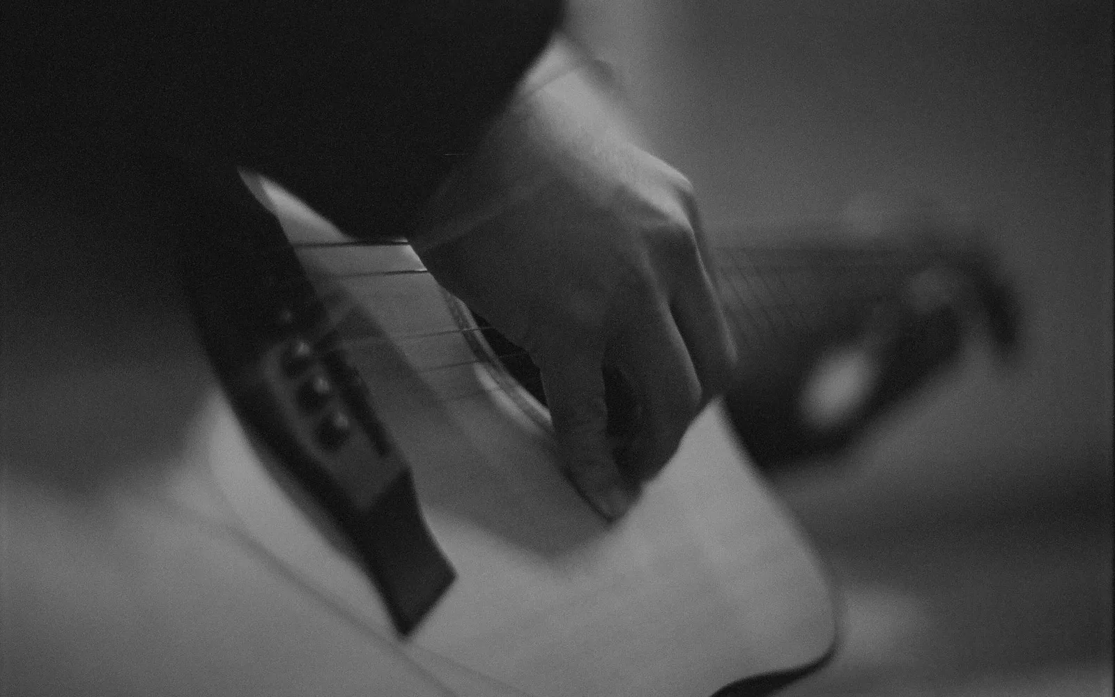Artistieke close-up van een hand die een akoestische gitaar tokkelt, wat een warme muzikale sfeer creëert