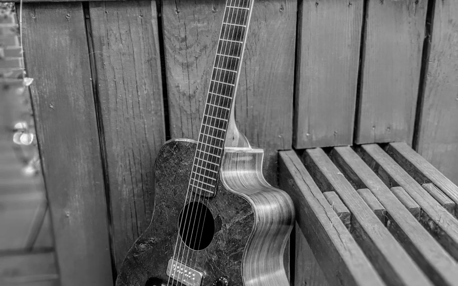 Chitarra acustica in legno appoggiata a una panca di legno all'aperto