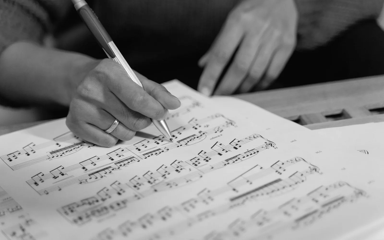 Uma mão escrevendo notação musical em uma folha de papel pautado
