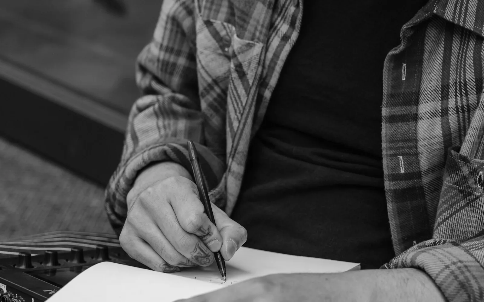 Ein Songwriter hält einen Stift über ein offenes Notizbuch neben Musikequipment