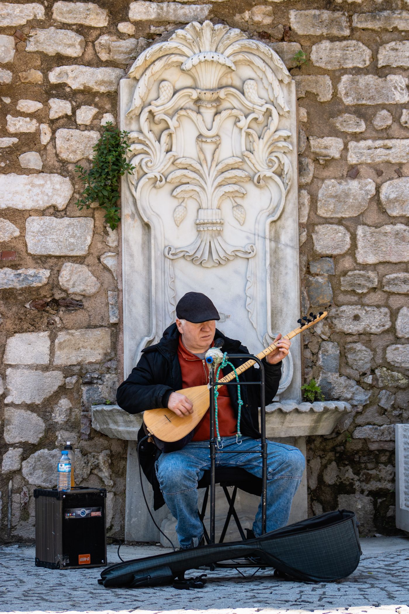 Ein Straßenmusiker spielt Saz vor einem steinernen Hintergrund