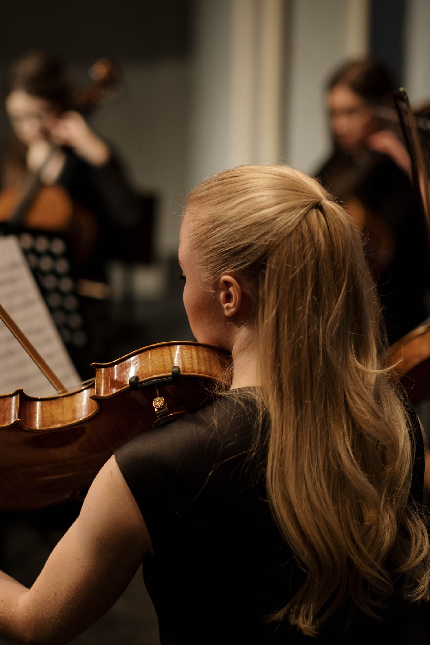 A violinist holding a bow while playing alongside other orchestral musicians