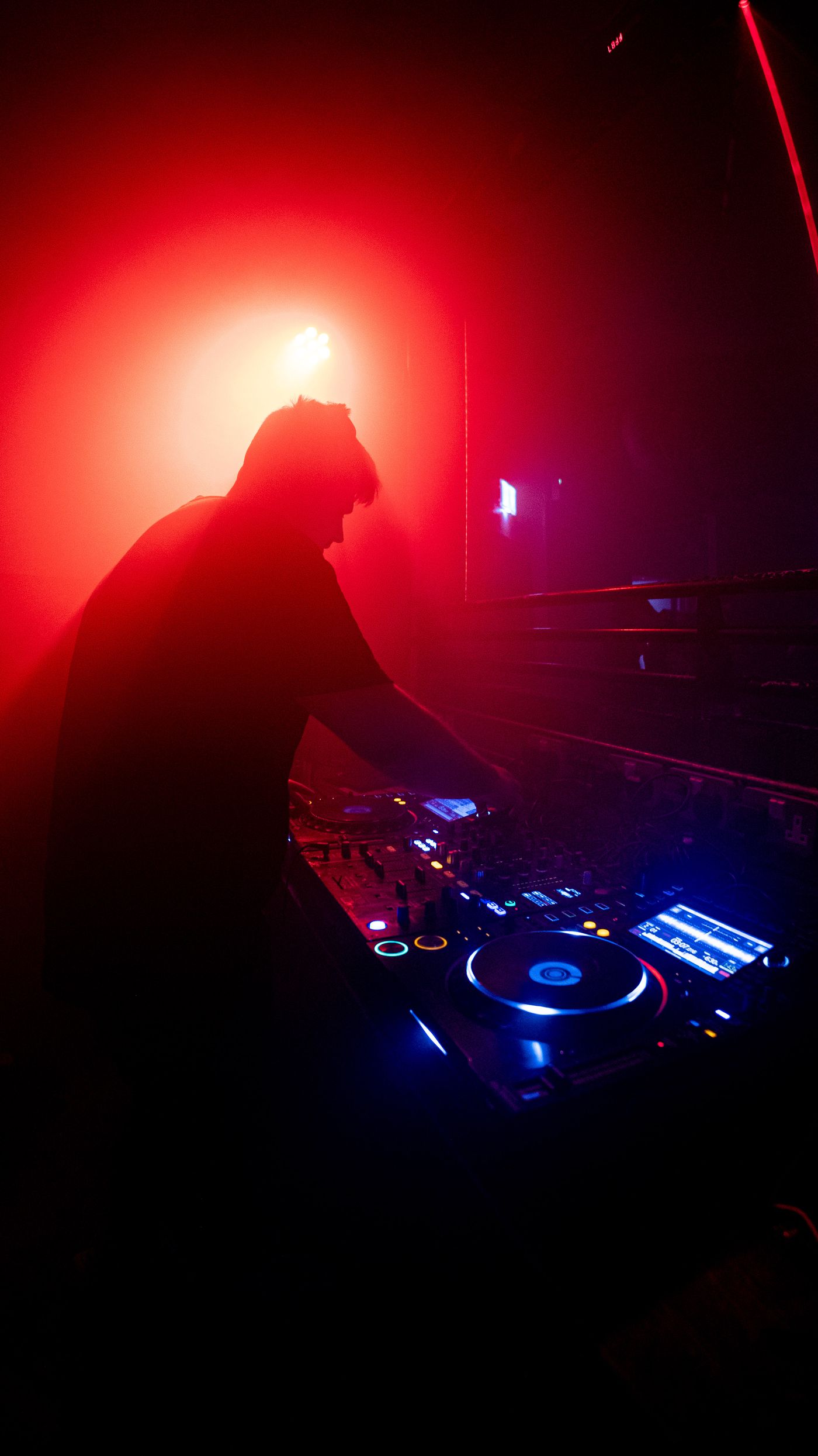 Silhouette eines DJs hinter einem Mischpult in einem dunklen Club