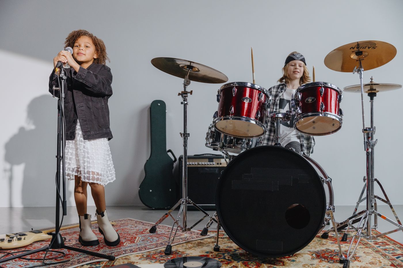 Due bambini che suonano la batteria e cantano in un microfono al chiuso