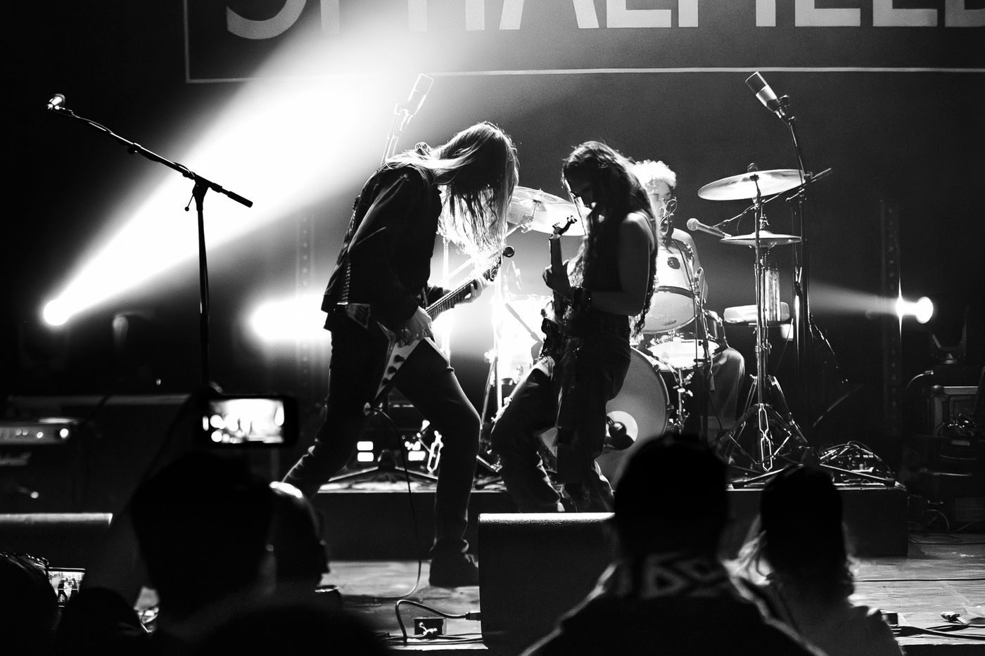 Guitarist and drummer performing with their band under stage lighting