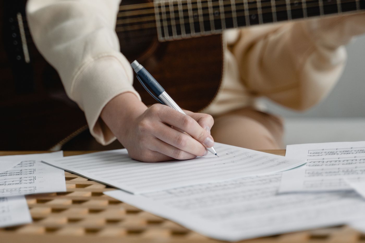 Eine Person, die Musik auf Papier neben einer Gitarre schreibt