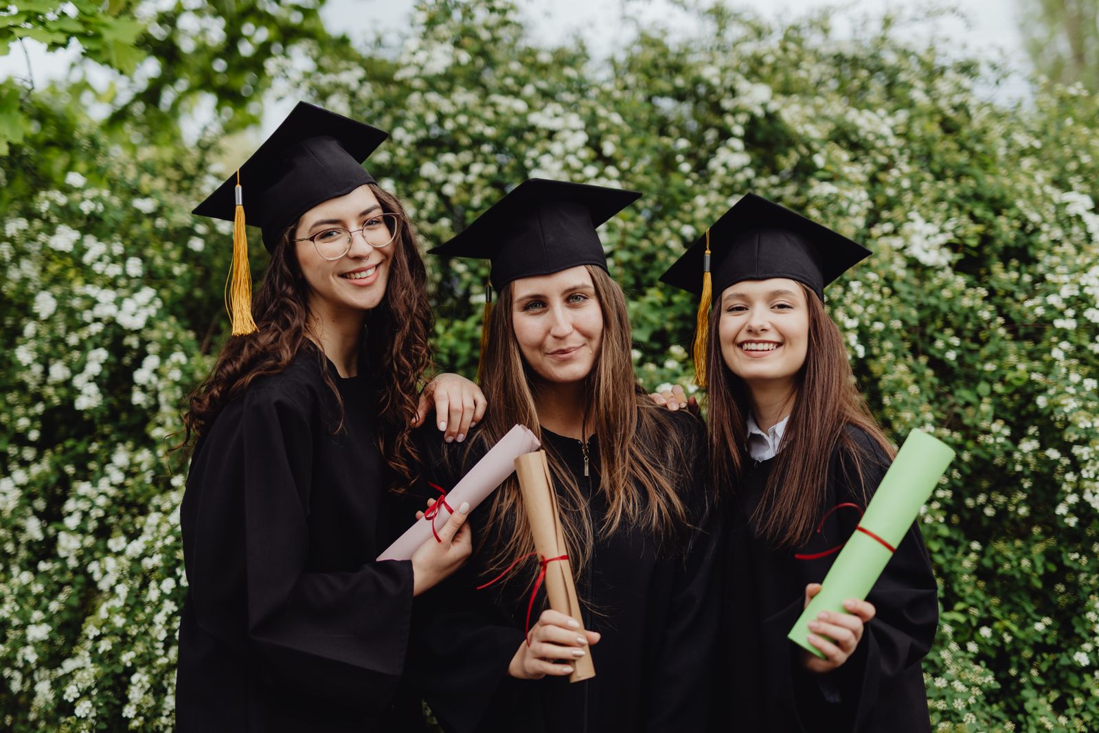 Graduates in caps and gowns holding their diplomas outdoors