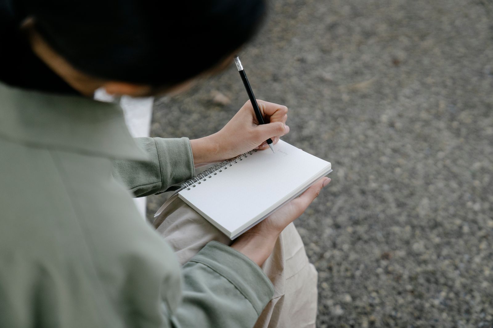 A person writing in a spiral notebook outdoors